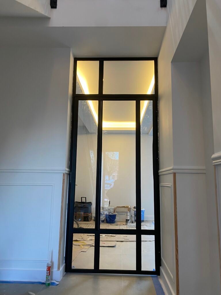 Porte vitrée avec cadre en métal noir donnant sur une pièce bien éclairée.