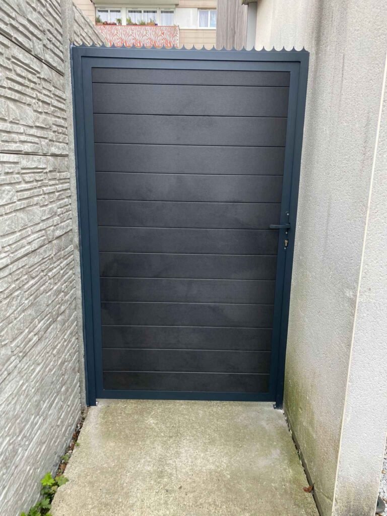 Un portail en aluminium gris foncé avec des lattes horizontales, installé entre deux murs texturés dans une allée étroite.